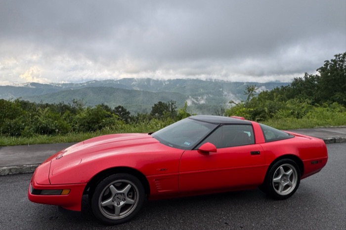 A red 1990s Chevrolet Corvette ZR-1 parked at a mountain overlook.
